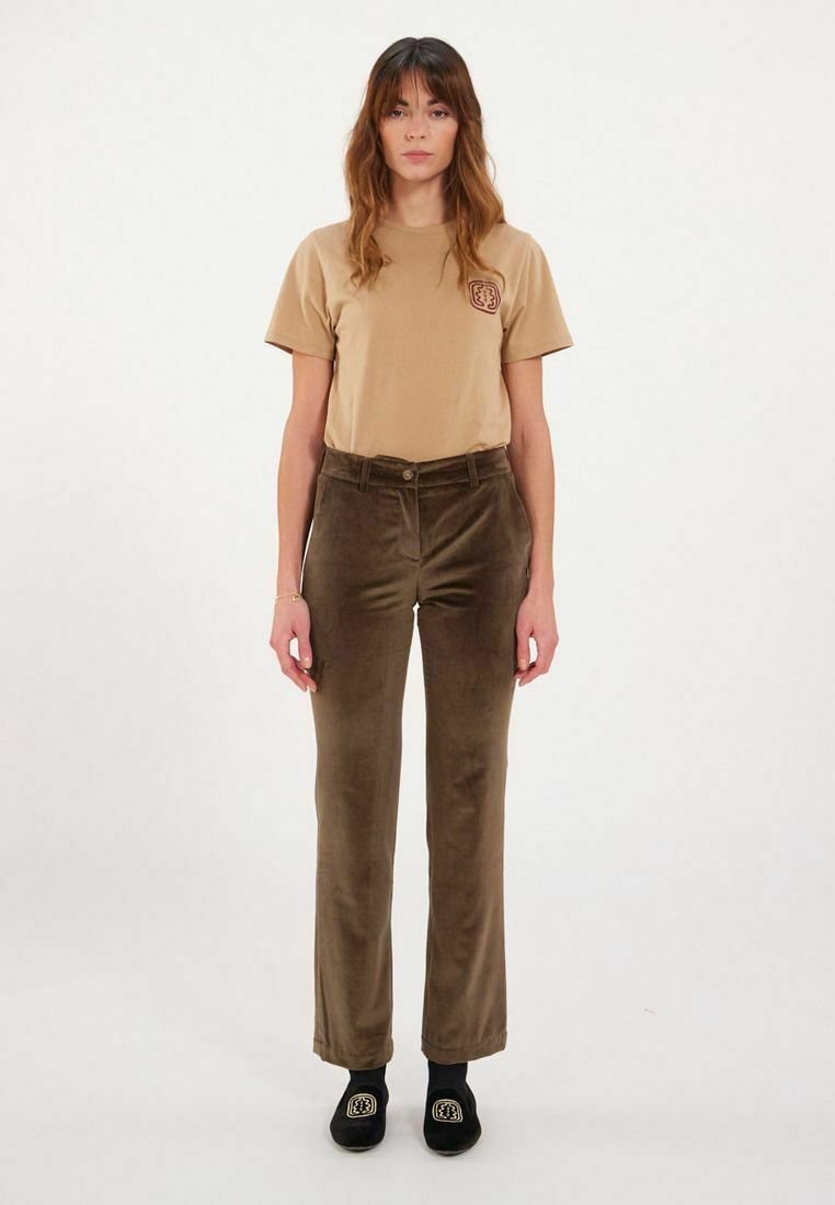 T-shirt marron clair avec un petit logo, associé à un pantalon en velours côtelé marron. Le modèle porte des chaussures noires à enfiler. Tenue simple et décontractée.