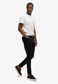 Camiseta blanca de algodón, jeans negros, puños enrollados, zapatillas negras con suelas crema, calcetines marrones, diseño casual. Sin patrones ni acentos visibles.