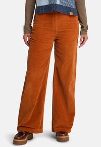 Corduroy wijde broekspijpen in levendig oranje, met verticale ribbels en een gestikte tailleband. Gepaard met bruine plateau schoenen.
