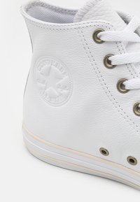 Białe wysokie trampki wykonane z teksturowanej skóry, z metalowymi oczkami, białymi sznurówkami i okrągłym logo z gwiazdą po boku.
