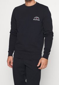 Sudadera navy de manga larga, cuello redondo y logo bordado "Tommy Hilfiger" en el pecho. Puños y dobladillo acanalados. Textura suave.
