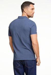 Polo de color azul marino hecho de suave algodón, con un cuello clásico y mangas cortas. La parte trasera presenta un diseño ajustado con una textura suave.