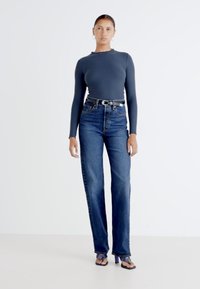 Haut à manches longues rayé bleu marine, jeans taille haute bleus et sandales à talons hauts. Texture lisse, coupe droite, design minimaliste.