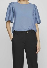 Haut bleu clair à manches courtes avec une finition texturée, encolure ronde et manches bouffantes, associé à un pantalon noir avec un détail de bouton.