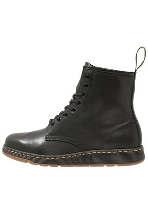 Bottine noire en cuir à lacets avec coutures jaunes, semelle à nervures et languette à l’arrière.
