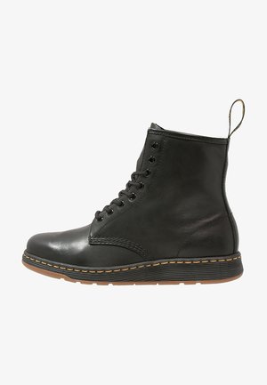 Bottine noire en cuir à lacets avec coutures jaunes, semelle à nervures et languette à l’arrière.