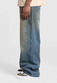 Lyseblå denimjeans med en afslappet pasform og en falmet tekstur. Har sidelommer og subtile syningsdetaljer. Bæret med mønstrede sneakers.