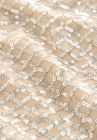 Beige szövet, ezüst flitterekből készült gyémánt mintával, amely texturált és fényvisszaverő felületet hoz létre. Puha, hálószerű minőség.