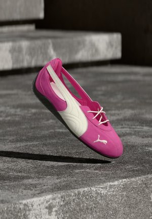Chaussure plate Puma rose et blanche avec des lacets reposant sur une marche en béton gris à l'extérieur.