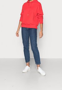 Rode hoodie met een relaxte pasvorm, gecombineerd met blauwe rechte jeans en witte sneakers. Soepele stof en simpel ontwerp.