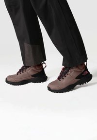 Zapatos de senderismo marrón claro con detalles en negro; suela de goma texturizada, diseño de cordones y marca visible en el talón. Listos para el sendero.