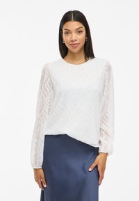 White textured blouse with long sleeves and a wave pattern. Paired with a dark blue satin skirt. Light and airy fabric.
