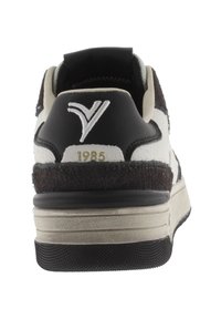 Sneaker con una toma in suede nero e bianco, dettagli testurizzati, un collare imbottito e un logo prominente con "1985" in oro sul tallone.