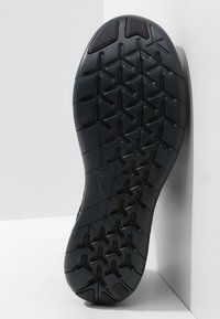 Semelle de chaussure de sport noire avec un motif de bande de roulement texturé et multidirectionnel, présentant des rainures angulaires et une section talon lisse.