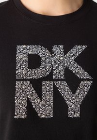 Schwarzes T-Shirt mit einem silbernen Strassdesign "DKNY", bei dem unterschiedlich große, funkelnde Steine für Textur und visuelles Interesse sorgen.