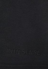 Juodas tekstilė su lygiu, megztu tekstūros paviršiumi. Audinyje apačioje įspaustas logotipas su užrašu "3NTM SENSE."