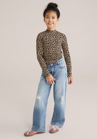 Leopardenmuster Langarmshirt, blaue, zerrissene, weite Jeans und pinke Schuhe mit weißen Schnürsenkeln. Das Outfit zeichnet sich durch eine figurbetonte Silhouette aus.