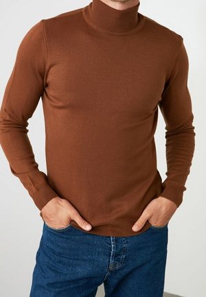 Brauner, langärmeliger Rollkragenpullover aus Rippstoff. Die enganliegende Passform betont den Oberkörper und wird mit blauen Jeans kombiniert.