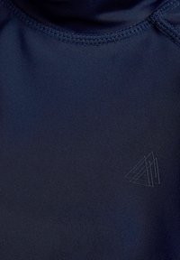 Mörkblå idrottströja med en slät yta, med flata sömmar och en subtil präglad logotyp i det nedre högra hörnet.