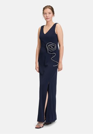 Robe ajustée bleu marine avec un décolleté en V, une fente sur le côté et une broderie en argent complexe formant un design en spirale sur la hanche. Tissu doux, sans manches.