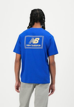 T-shirt en coton bleu avec un grand logo doré "New Balance" au dos. Manches courtes, col rond et coupe décontractée.