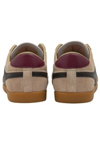 Un paio di sneakers beige in suede con suole marroni, strisce laterali nere e toppe sul tallone color bordeaux, viste da dietro.