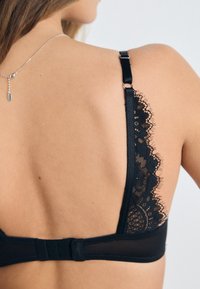 Black lace-back bra featuring a delicate scalloped lace trim and adjustable straps, with a hook-and-eye closure at the back for fit.