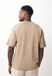 Beež värvi puuvillane T-särk lühikeste varrukatega, lõdva istuvusega ja ümar kaelusega. Sile tekstuur, minimaalsete õmblustega ja ilma nähtavate mustriteta.