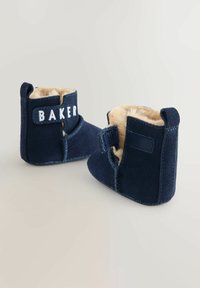 Tmavomodré semišové čižmičky s mäkkou béžovou kožušinovou podšívkou, suchým zipsom a výšivkou „BAKER“ na prednej strane. Zaoblená špička a pevná podrážka.