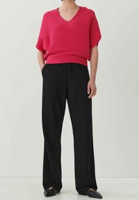 Fuchsiový pletený svetr s výstřihem do V a krátkými rukávy, spárovaný s volnými černými kalhotami. Celkově uvolněný střih, hladká textura a minimální detaily.