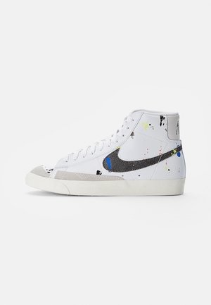 Weißer High-Top-Sneaker mit schwarzem Nike-Swoosh und bunten Farbspritzern, beigen Akzenten und weißer Gummisohle vor einfachem Hintergrund.