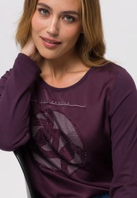 Paars langekm shirt met een cirkelvormig gaaspatroon en sprankelende accenten, voorzien van een ronde hals en een zachte textuur.