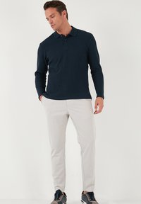 Polo de manga larga azul marino con cuello, combinado con pantalones beige claros y zapatillas oscuras. Textura suave, diseño ajustado.