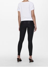 Svarta leggings med ett mönster av leopardfläckar, kombinerat med en vit kortärmad t-shirt. Outfitten har en slät textur och en åtsittande design.