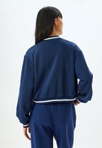 Marinblå kort sweatshirt med ribbade vita och marinrandiga detaljer vid kragen och ärmsluten. Slät textur och avslappnad passform.