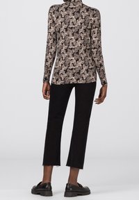 Svart långärmad topp med en texturerad beige mönster, i kombination med svarta cropped byxor och klumpiga svarta skor, sedd från baksidan.