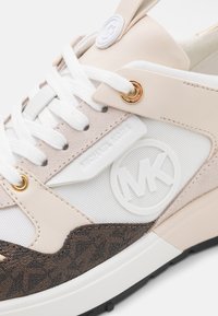 Sneaker met een combinatie van beige leer en suède, witte mesh, gouden accenten en een bruin patroonpaneel met een reliëflogo.