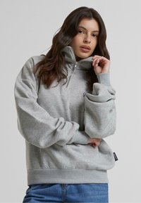 Sudadera gris con un alto cuello y cierre de cuarto de cremallera. Presenta puños y dobladillo de canalé, fabricada con un tejido suave y elástico, con un corte relajado.