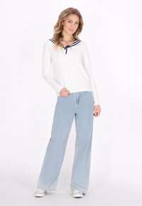 Top bianco a maniche lunghe con colletto da marinaio a strisce blu navy, abbinato a jeans a gamba larga azzurri e sneakers bianche.