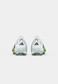 Des chaussures de football blanches avec des accents noirs et jaunes fluo, présentant une surface lisse et brillante ainsi que des crampons moulés pour une meilleure traction.