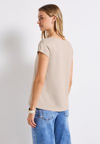 Haut beige à manches courtes avec un col rond, texture douce et coupe décontractée ; associé à un jean en denim bleu clair.