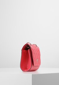 Červená texturovaná kabelka s klopou, stříbrným kováním a strukturovaným tvarem. Má reliéfní vzor a hladké boční panely.