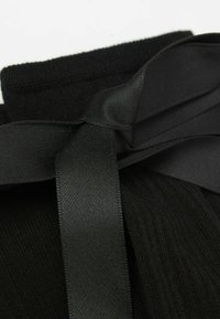Calcetines negros acanalados están atados con una cinta negra lisa, mostrando una textura suave y un diseño elegante. El color es uniforme en toda su extensión.