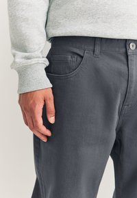 Ciemnoszare spodnie wykonane z gładkiej, fakturowanej tkaniny, z przednimi kieszeniami i prostym krojem, zestawione z jasnoszarym swetrem.