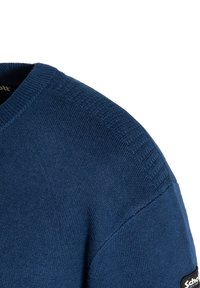 Blauer Strickpullover mit ribbeligem Rundhalsausschnitt und strukturierten Akzenten an der Schulter. Verfügt über ein kleines Logopatch an der Seite.