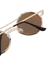 Kulaté sluneční brýle s bronzovými skly, tenký zlatý kovový rámeček, černé plastové nožičky a průhledné nosní podložky. Slim design s dvojitým mostem.