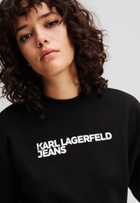 Black cotton sweatshirt featuring bold white text "KARL LAGERFELD JEANS" across the front, with a crew neck and relaxed fit.