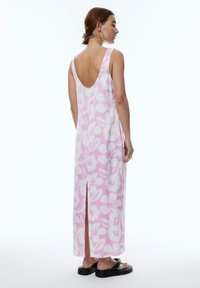 Ärmelloses, pinkes, blumengemustertes Maxikleid mit tiefem Rückenausschnitt und seitlichem Schlitz, aus leichter Stoffqualität, kombiniert mit schwarzen Sandalen.