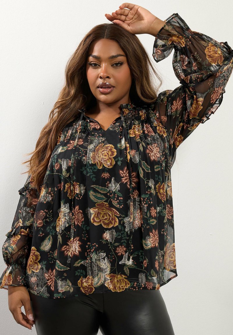 Blusa floreale in tessuto nero trasparente, con maniche lunghe arricciate e vestibilità rilassata, decorata con motivi colorati di rose e foglie.