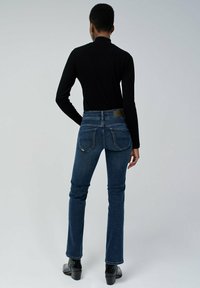 Jeans de mezclilla de tiro alto, de color azul oscuro, con un corte slim y un ligero acampanado, que cuentan con bolsillos traseros y un parche de cuero liso en la cinturilla.